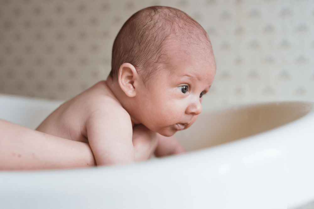A newborn being held in a baby bath.